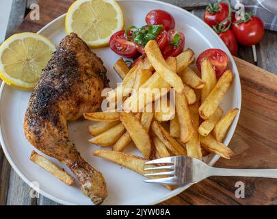 Knusprige Hühnerschenkel mit hausgemachten pommes Frites und Tomatensalat Stockfoto