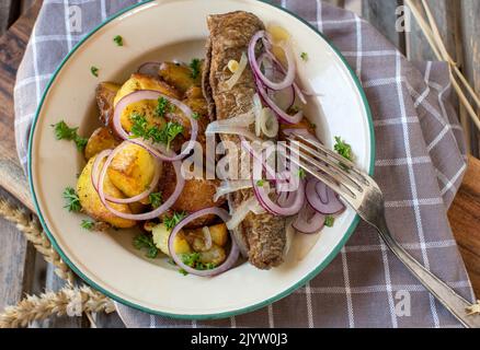 Gebratener Hering und gebratene Kartoffeln auf einem altmodischen emaillierten Teller Stockfoto