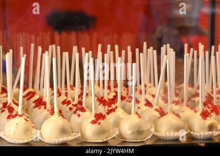 Reihen von kleinen Süßigkeiten auf Stäbchen, die mit weißer Schokolade überzogen sind. Keine Personen. Stockfoto