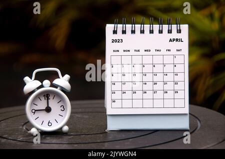 Wecker zeigt auf 9 Uhr mit Kalender vom 2023. April auf verschwommenem Parkhintergrund. Zeit- und Kalenderkonzept. Stockfoto