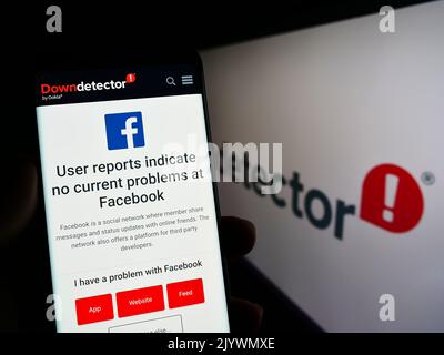 Person, die Smartphone mit Website der Plattform Downdetector und Facebook-Status vor dem Logo hält. Konzentrieren Sie sich auf die Telefonanzeige. Stockfoto