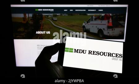Person mit Mobiltelefon und Logo des US-Unternehmens MDU Resources Group Inc. Auf dem Bildschirm vor der Business-Webseite. Konzentrieren Sie sich auf die Telefonanzeige. Stockfoto