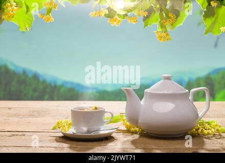 Lindentee auf dem Gartentisch. Teekannen und Becher auf Holztisch. Lindenblüten und heißer Limetttee. Kräutertees-Konzept. Stockfoto