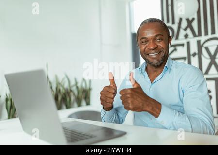 Lächelnder afrikanischer Geschäftsmann zeigt erhobene Finger auf, während er im Büro sitzt Stockfoto