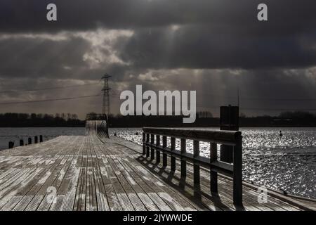 Stürmische Wolken über einem Pier und einem dunklen See Stockfoto