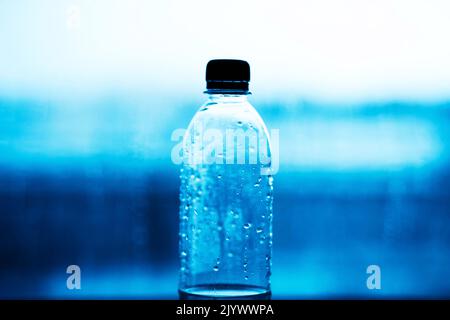 Eine Plastikflasche mit einem schwarzen Deckel, der halb mit sauberem Wasser gefüllt ist, steht vor dem Hintergrund von blauem Wasser. Plastikverschmutzung des Ozeans. Trinken w Stockfoto