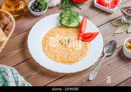 Köstliche appetitliche Erbsenbrei garnieren Sie mit frischem Gemüse auf einem weißen Teller auf einem Holzhintergrund Stockfoto