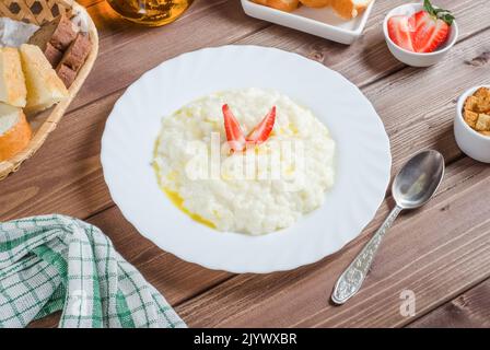 Köstlicher Reismilchbrei mit Butter und Erdbeeren auf einem weißen Teller auf dunklem Holzboden. Stockfoto