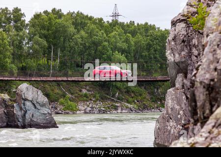 Altai, Russland - 08. 20. 2022: Red Haval Jolion fährt auf einer hölzernen Hängebrücke über den Fluss zwischen den Felsen Stockfoto