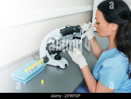 Laborwissenschaftler, der im Labor mit Mikropipette, Reagenzgläsern und modernem Mikroskop arbeitet. Laborforschung, Mikrobiologie Stockfoto