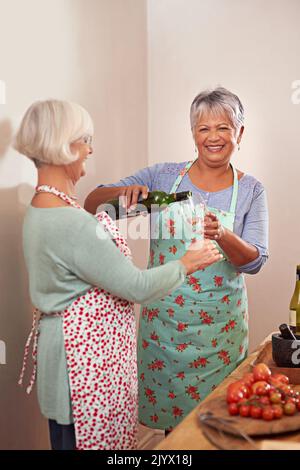 Und ein Spritzer für uns. Zwei ältere Frau, die beim Kochen Wein trinkt. Stockfoto