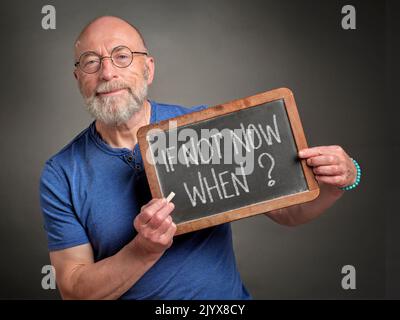 Wenn nicht jetzt, wann? Ein älterer Mann, Lehrer, Moderator oder Mentor hält eine Schiefertafel mit weißem Kreidetext in der Hand. Aufruf zu Aktion, Bildung und Kommunikation Stockfoto