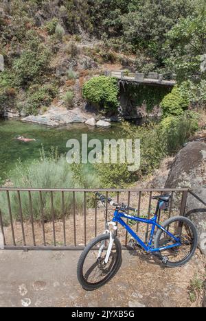 MTB-Fahrrad neben dem natürlichen Schwimmbad La Maquina, Guijo de Santa Barbara, Spanien. Toller Ort für Triathlon-Praktizierende Stockfoto