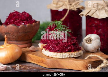 Hausgemachter würziger Kaviar aus Rüben, Karotten, Zwiebeln und Knoblauch auf geröstetem Brot und auch in Gläsern auf Holzbrett auf hellgrauem Hintergrund Stockfoto