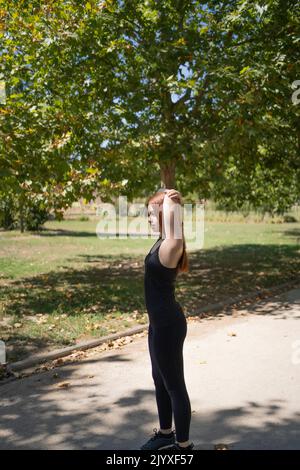 Attraktive junge Rotschopf Frau trägt schwarze Sportkleidung dabei Übungen Stockfoto