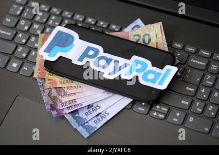 TERNOPIL, UKRAINE - 6. SEPTEMBER 2022 Paypal-Papier-Logo liegt auf schwarzer Laptop-Tastatur mit brasilianischen Reals Rechnungen. Payoneer ist ein US-amerikanischer Finanzdienstleister Stockfoto