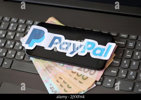 TERNOPIL, UKRAINE - 6. SEPTEMBER 2022 das Paypal-Papierlogo liegt auf der schwarzen Laptop-Tastatur mit ukrainischen Griwna-Rechnungen. Payoneer ist ein amerikanischer Finanzdienstleister Stockfoto