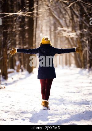 Eine Frau, die ihre Arme bei einer Wanderung durch den Wald im Winter bei Sonnenuntergang ausstreckt. Stockfoto