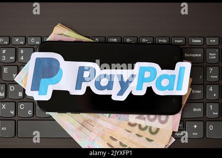 TERNOPIL, UKRAINE - 6. SEPTEMBER 2022 das Paypal-Papierlogo liegt auf der schwarzen Laptop-Tastatur mit ukrainischen Griwna-Rechnungen. Payoneer ist ein amerikanischer Finanzdienstleister Stockfoto