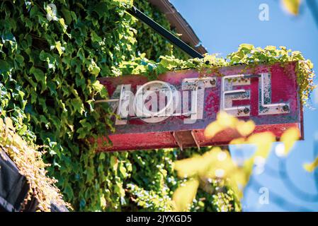 Ein rustikales Motelschild von unten, das mit Efeu bedeckt ist, außerhalb der Innenstadt von San Luis Obispo, Kalifornien, an einem Sommertag. Stockfoto