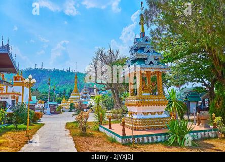 Der hohe goldene Chedi des Wat Chong Klang Temple, gekrönt mit einem hti-Regenschirm, ist hinter dem Garten und dem mondop-Schrein des Wat Chong Kham Temple, Mae Ho zu sehen Stockfoto