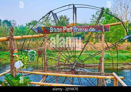 PAI, THAILAND - 6. MAI 2019: Beobachten Sie am 6. Mai in Pai das sich drehende hölzerne Wasserrad am Pai-Fluss mit üppigem Grün am gegenüberliegenden Ufer Stockfoto