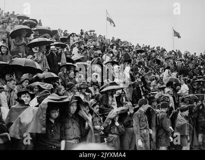 Empire Games Athletics, Final Day, Eden Park, Auckland. Februar 11. Zuschauer auf dem offenen Stand im Eden Park trotzen dem sintflutartigen Regen mit Regenschirmen und improvisierten Schutzräumen. 14. Juni 1950. Stockfoto