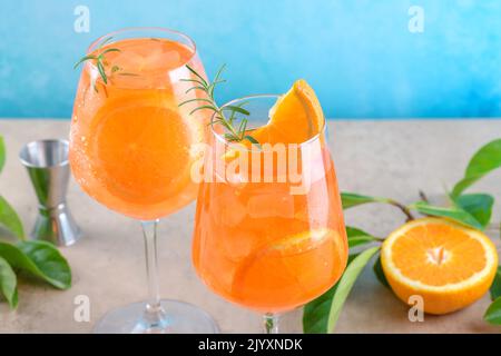 Klassischer italienischer Aperitif aperol Spritz Cocktail in zwei Weinläsern mit Eiswürfeln und Orange-Scheibe mit hellblauem Hintergrund auf beigefarbenem Steinhintergrund Stockfoto