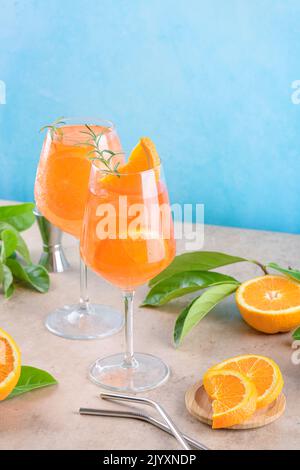 Klassischer italienischer Aperitif aperol Spritz Cocktail in zwei Weinläsern mit Eiswürfeln und Orange-Scheibe mit hellblauem Hintergrund auf beigefarbenem Steinhintergrund Stockfoto