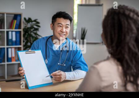 Froh reifen asiatischen Mann Arzt zeigen Dokument zu tausendjährigen schwarzen weiblichen Patienten in Klinik Büro Innenraum Stockfoto