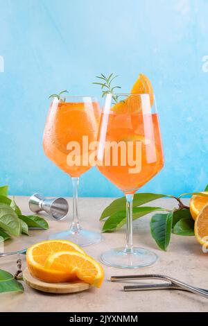 Klassischer italienischer Aperitif aperol Spritz Cocktail in zwei Weinläsern mit Eiswürfeln und Orange-Scheibe mit hellblauem Hintergrund auf beigefarbenem Steinhintergrund Stockfoto