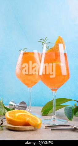 Klassischer italienischer Aperitif aperol Spritz Cocktail in zwei Weinläsern mit Eis und Orangenscheibe mit hellblauem Hintergrund auf beigefarbenem Steingrund, Stockfoto