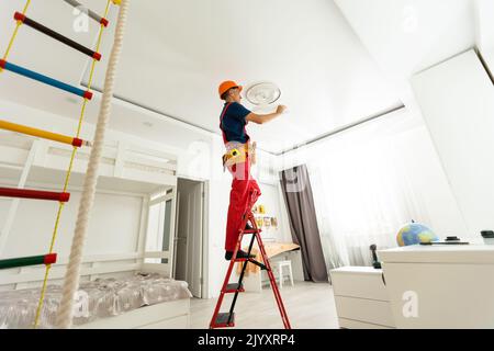 Junger Mann repariert die Kabelverkabelung und installiert oder ersetzt die Halogenlampe an der Decke. Stockfoto