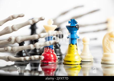 Schach mit einer gemalten Flagge Russlands und der Ukraine auf einem Schachbrett und einer Hand eines Skeletts auf dem Brett, dem Todesspiel der beiden Länder der Ukraine Stockfoto