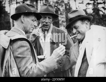 Eine Pause in der Königlichen Elchjagd Foto zeigt: König Frederick (links) zündet Kronprinz Olavs Zigarette an. Prinz Wilhelm schaut zu. Prinz Wilhelm von Schweden war Gastgeber einer königlichen Elchjagd in Halle und Hunneberg, in der Nähe von Uddevalla, Schweden, im September 27. Unter den Gästen waren König Fredrick von Dänemark und Kronprinz Olav von Norwegen. König Friedrich schoss drei Bullen, Kronprinz Olav schoss einen Bullen und Prinz Wilhelm schoss eine Kuh und einen Bullen. 08. Oktober 1952. (Foto von Associated Press Photo) Stockfoto