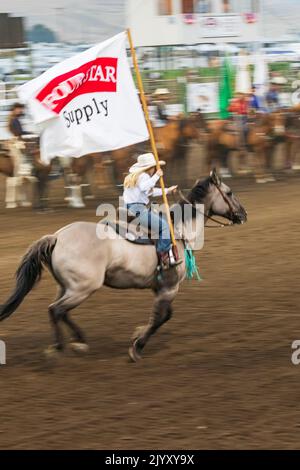 USA, Washington State, Whitman County. Palouse. Palouse Empire State Fair. Colfax. 9. September 2021. Frau, die bei einem Rodeo mit Flagge reitet. Stockfoto