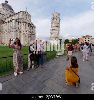 Platz der Wunder in Pisa, Toskana, Italien. Touristen posieren für Fotos vor dem Schiefen Turm von Pisa. Kathedrale links. Stockfoto