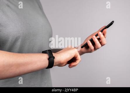 Frau mit Fitnessarmband am Handgelenk, die die mobile App am Telefon nutzt, um die Ergebnisse der körperlichen Aktivität zu überprüfen oder Uhren mit dem Smartphone zu verbinden. Gesunde Lif Stockfoto