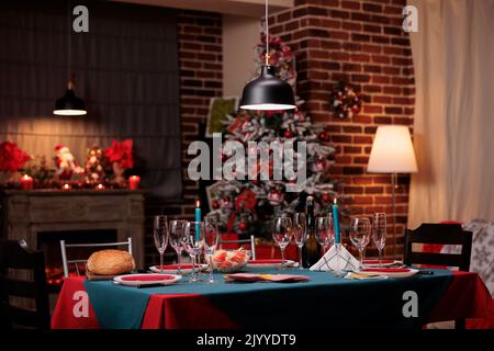 Weihnachtsabend Tisch in Luxus-Interieur, schön dekorierten Ort, Winter saisonalen Feiertagen traditionellen Vorbereitungen. Leere Weingläser, Essteller, Kerzen auf der Tischplatte, Tannenbaum Stockfoto