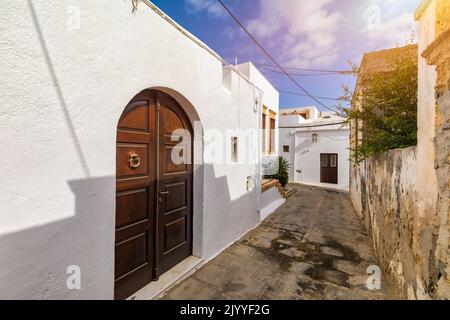 Schmale Straße in Lindos Stadt auf Rhodos Insel, Dodekanes, Griechenland. Schöne malerische Lindos alte alte weiße Häuser mit Blumen. Berühmte touristische Desti Stockfoto