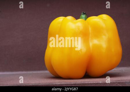 Big Yellow Paprika Sweet Pepper mit grünem Stiel auf der braunen Haussteinstufe. Seitenansicht, Nahaufnahme, Makro Stockfoto