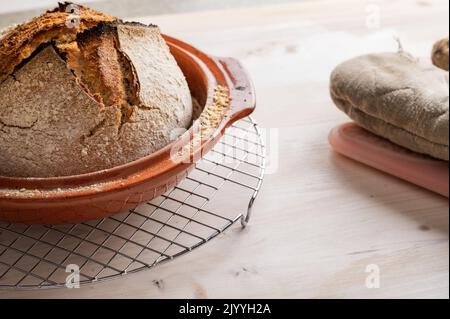 Köstliches hausgemachtes Sauerteig-Brot, frisch gebacken in einem Tontopf auf Holzbrett. Stockfoto