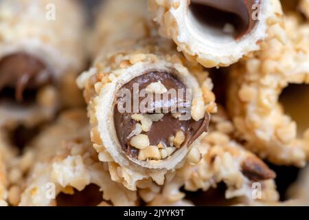 Waffelröhrchen mit Schokoladenfüllung und zerkleinerten Erdnüssen, süße Waffelröhrchen mit frittierten Erdnussstücken mit Schokoladenfüllung Stockfoto