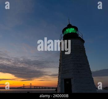 Newport Harbor Lighthouse alias Goat Island Light House bei Nacht mit grüner Leuchtfeuer und der Claiborne Pell Newport Bridge, Newport, Rhode Island. Stockfoto