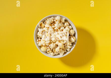 Popcorn in einer weißen Schüssel auf gelbem Hintergrund. Blick von oben. Stockfoto