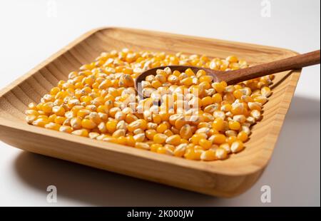 Getrocknete Maiskörner in Holzschüssel auf weißem Hintergrund platziert. Mais für Popcorn. Stockfoto