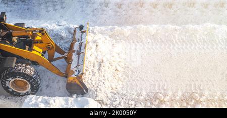 Ein großer orangefarbener Traktor entfernt Schnee von der Straße und räumt den Bürgersteig frei. Reinigung und Räumung der Straßen in der Stadt vom Schnee im Winter. Schneeräumung A Stockfoto