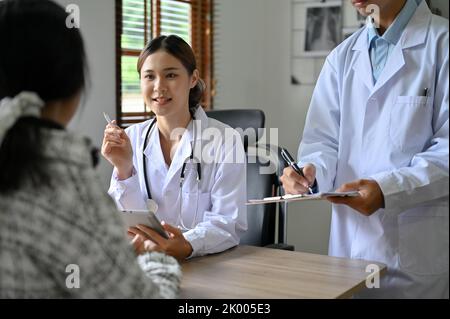 Professionelle und erfahrene asiatische Ärztin und ihre Assistentin im Untersuchungsbüro, besprechen den Operationsplan und geben ihrer Patie einen Rat Stockfoto