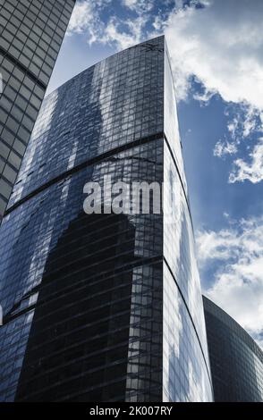 Selektiver Fokus, Fragment von transparenten glasigen Wänden des Wolkenkratzers, der den Himmel mit Wolken reflektiert.Moderne Architektur, umweltfreundliche Technologien und Engi Stockfoto