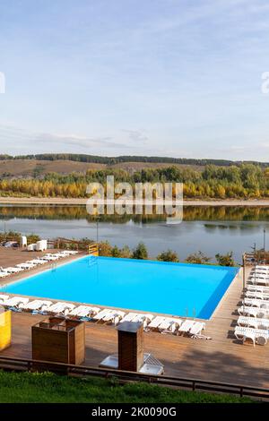 Blauer Pool ohne Menschen am Flussufer im Herbst. Ein großartiger Ort zum Entspannen und Entspannen in der Natur. Der Pool und die Sonnenliegen warten auf Besucher Stockfoto